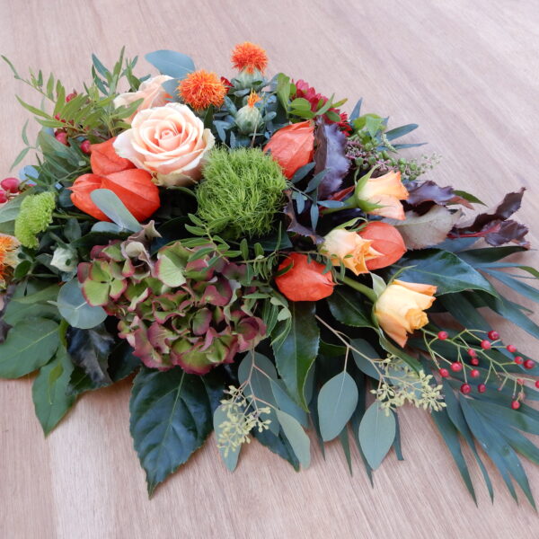 Rouwstuk oranje met hortensia en diverse bladmateriaal.
